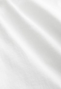 Valkoinen puuvillakangas, jolla on sileä pinta, näyttää lieviä aaltoja ja hienovaraista kudontakuviota. Vaalea ja neutraali väri.