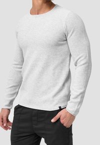 Light gray long-sleeve shirt made of textured fabric, featuring a round neckline and a small black tag at the hem. Paired with black pants.