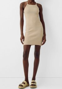 Robe en tricot côtelé beige à fines bretelles, silhouette ajustée et accents pastels. Associée à des sandales à plateforme beiges ornées d'une boucle décorative.