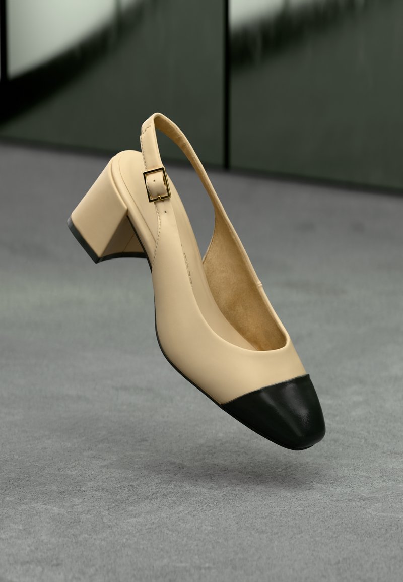Pompe à talon slingback en cuir beige avec un bout noir, petit talon carré et détail de boucle carrée dorée. Texture lisse, design minimaliste.