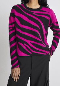 Maglione a collo rotondo con base nera e audaci strisce zebrate rosa. Realizzato in un materiale morbido e dotato di maniche lunghe.