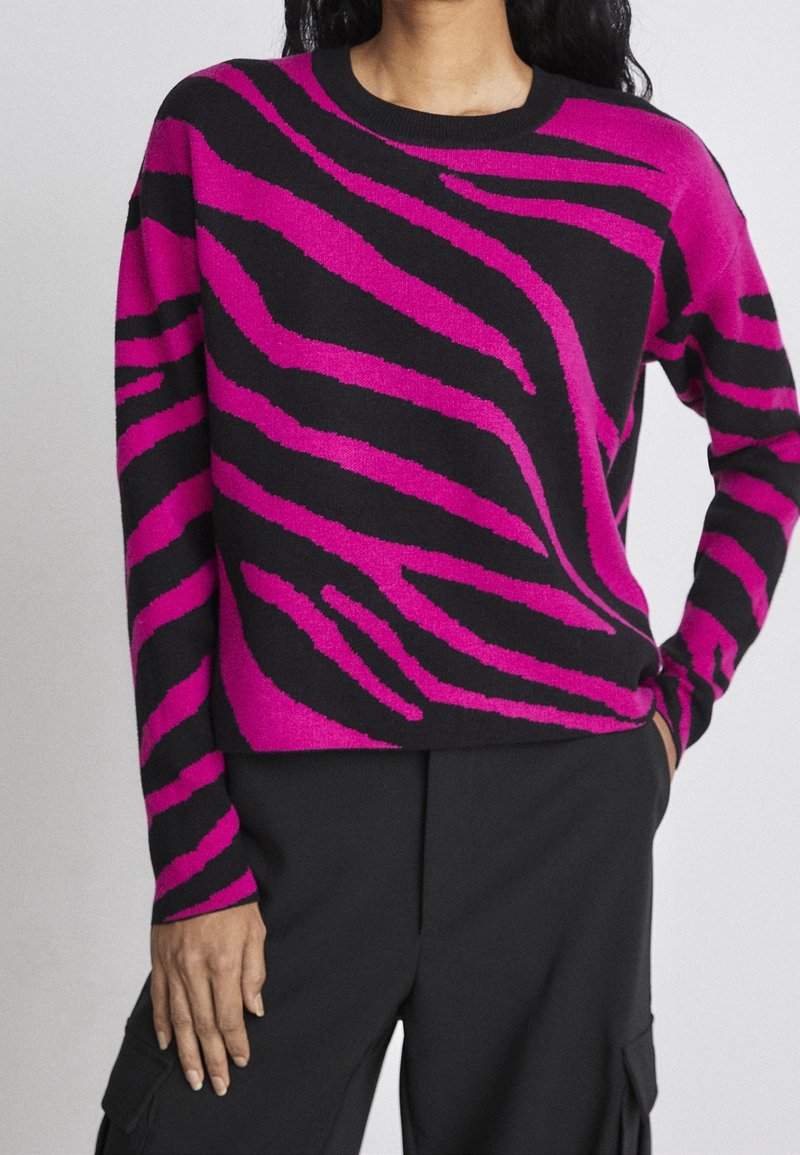 Maglione a collo rotondo con base nera e audaci strisce zebrate rosa. Realizzato in un materiale morbido e dotato di maniche lunghe.