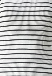 Top acanalado en blanco con rayas horizontales negras. La tela tiene una apariencia texturada, proporcionando un ajuste ceñido.