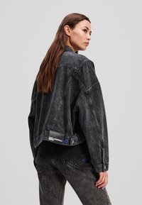 Veste en denim noir à coupe décontractée, avec une texture abîmée, des coutures marquées et un patch logo dans le dos.