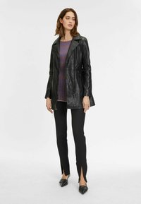 Zwarte leren jas met een gekarteld kraag, gecombineerd met een gestreept shirt en zwarte broek met zijsplitten. Gepunte flats maken de look compleet.