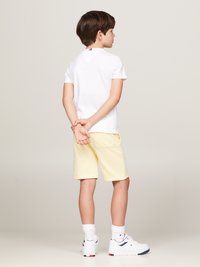 T-shirt blanche à manches courtes avec un col à rayures rouges et navy, associée à un short jaune et des baskets blanches. Design simple, coupe décontractée.