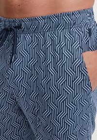 Marineblauwe shorts met een geometrisch wit patroon, voorzien van een elastische tailleband, koord en zijzak. Zacht, lichtgewicht materiaal.