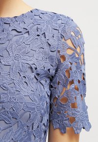 Tejido azul bordado con flores y detalles de corte en las mangas cortas, que muestra patrones de flores intrincados y una capa subyacente suave.
