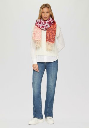 Écharpe en imprimé animal multicolore avec des nuances de rose et d'orange, ornée de franges, enroulée autour du cou du modèle qui porte un pull léger.