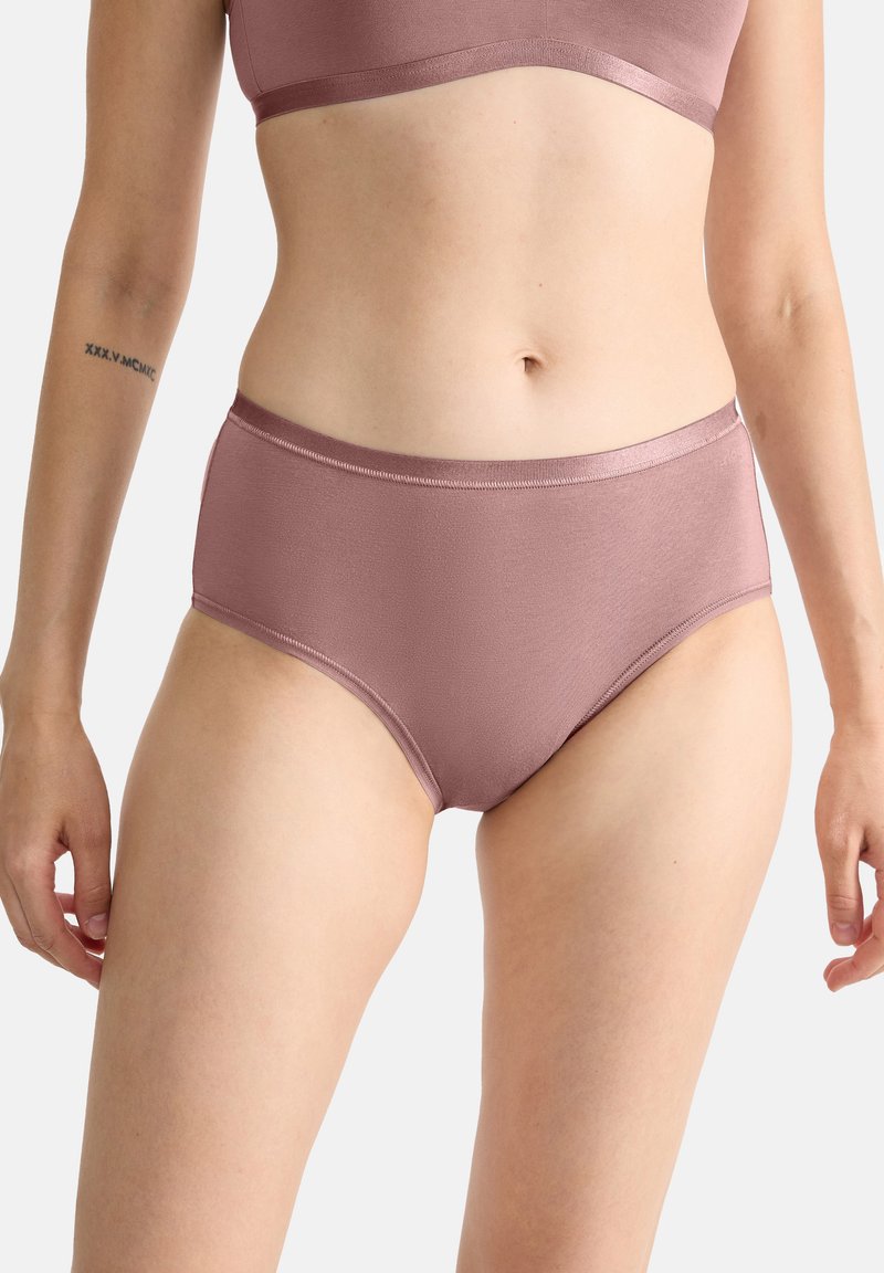 Femme portant des sous-vêtements sans couture mauve taille haute et un soutien-gorge assorti, montrant le ventre et le haut des cuisses sur un fond uni.