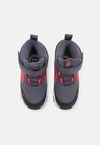 Graue und rote Kleinkinderschuhe mit einem Klettverschluss, gepolstertem Innenraum, runder Zehenpartie und weißer Sohle. Merkmale sind kontrastierende Akzente und ein Logo.