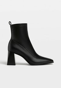 Botte noire en cuir avec bout pointu, talon bloc et languette à l'arrière, vue de profil sur un fond uni.