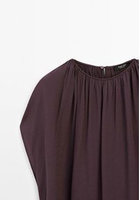 Blouse violet foncé avec encolure froncée et petite fermeture à bouton au col arrière, présentée sur fond blanc.