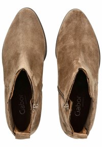 Braune Wildleder-Ankle-Boots mit einem Reißverschluss, spitz zulaufender Zehenpartie und flacher Sohle. Das Innere ist mit einer strukturierten Oberfläche versehen, auf der der Markenname sichtbar ist.