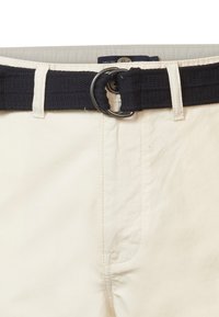 Pantaloni di cotone beige con una cintura artigianale blu navy dotata di una fibbia metallica rotonda. Il tessuto è liscio, con una texture sottile e cuciture laterali.