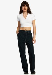 Witte korte mouwen crop top met een V-hals, gecombineerd met hoge zwarte broek met contrasterende witte stiksels en een rechte pijp.