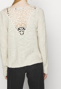 Stickad tröja i ljuskräm med V-formad rygg som har blommig spetsdetalj och texturerad tyg. Långa ärmar och avspänd passform.