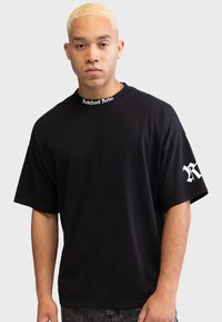 Czarna T-shirt z krótkim rękawem wykonana z bawełny, z okrągłym dekoltem i napisem "Redefined Rebel" oraz białym logo na lewym rękawie.