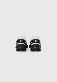 Zwart-witte sportschoenen hebben een hybride ontwerp met gebogen uitsparingen, een gevoerde kraag en textuurzolen met groene en rode accenten.