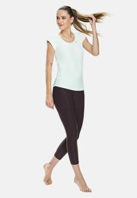 Hvid top med korte ærmer parret med sorte cropped leggings, begge lavet af strækbart stof. Toppen har et diskret logo-accent.