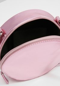 Bolsa redonda rosa con un acabado brillante, cierre superior con cremallera y un interior de tela negra. Presenta una textura suave y detalles de costura mínimos.