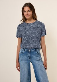 T-shirt bleu marine à manches courtes avec un motif blanc tourbillonnant. Associé à un jean taille haute bleu clair. Coupe décontractée, tissu doux.