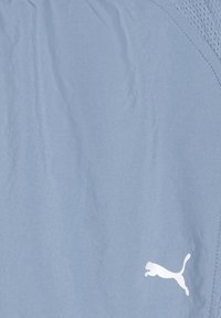 Gaiši zili sporta šorti no gludas auduma, ar sieta paneļa ieliktni. Uz kreisās puses ir redzams balts Puma logo.