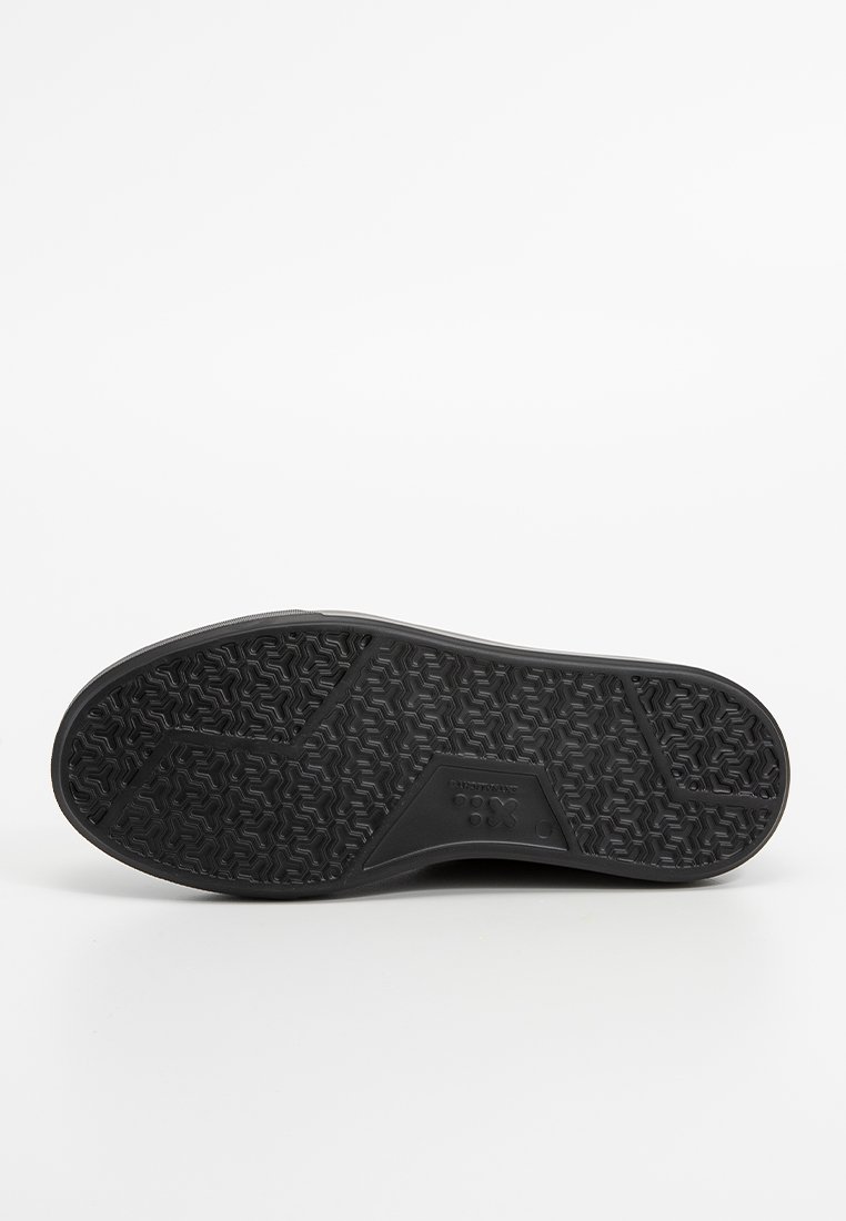 Suela de zapato de goma negra con un patrón de agarre texturizado, que presenta una zona de punta suave y un detalle de logo en el lateral.