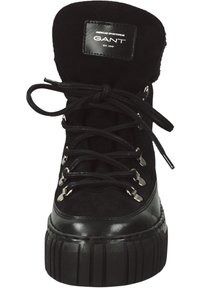 Schwarze Knöchelstiefel mit Obermaterial aus Wildleder, robuster Gummisohle und silbernen Beschlägen. Merkmale sind dicke Schnürsenkel und ein gepolsterter Kragen mit Logo.