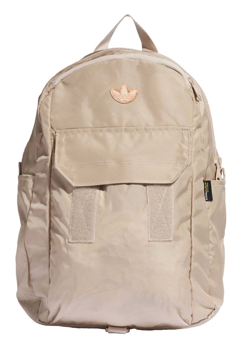 Khaki backpack with a smooth fabric, zip closure, front patch pocket, and a stitched emblem at the top center. Features side straps.