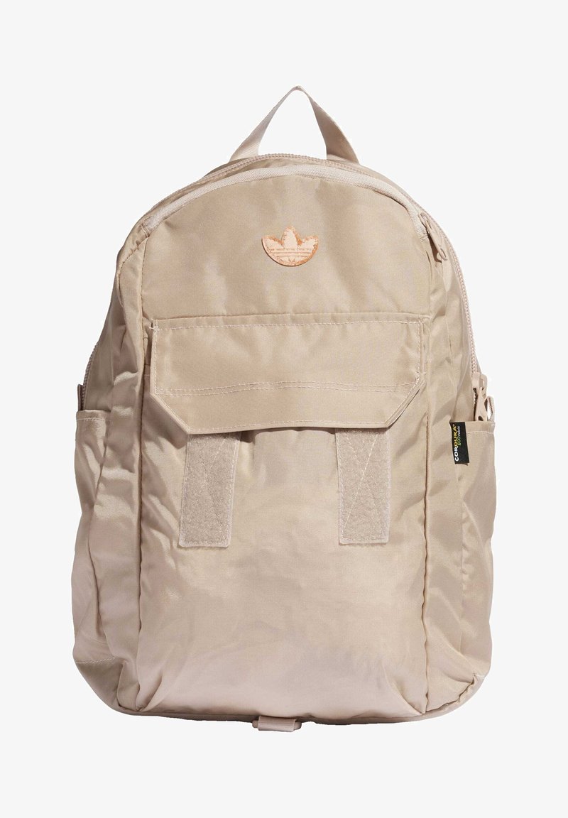 Khaki backpack with a smooth fabric, zip closure, front patch pocket, and a stitched emblem at the top center. Features side straps.