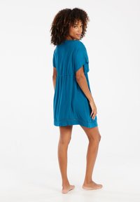 Minkštas tamsiai žalias medvilninis suknelė su laisvomis rankovėmis ir surinkta liemeniu. Yra apvalus iškirpimas ir sijono apdaila su mažais siuvinėjimo akcentais.