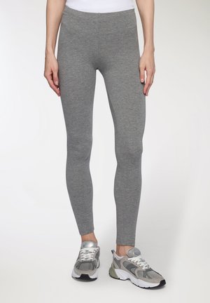 Leggings grigi con un tessuto elasticizzato e un design aderente. Presentano una vita elastica e una texture liscia. Indossati con sneakers grigie e bianche.