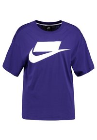 Fioletowa koszulka Nike z krótkim rękawem z dużym białym, stylizowanym logo swoosh na klatce piersiowej.