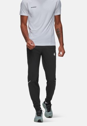 Black athletic pants with reflective accents, paired with a white short-sleeve shirt. Model wearing light blue running shoes.