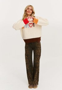 Gruba kremowa sweter z kolorowym haftem "amore", w połączeniu z brązowymi spódnicami w leopardzie cętki i brązowymi butami.