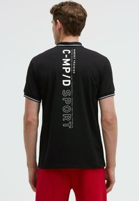 Polo negro con un estampado gráfico blanco en la parte posterior, con acentos de color contrastante en el cuello. Fabricado en una tela suave y transpirable.
