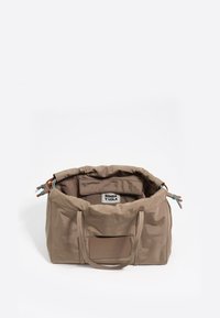 Bolsa de tela beige con cierre de cuerda. Cuenta con asas resistentes, un bolsillo interior y una etiqueta de logo. Textura suave con un diseño sencillo.