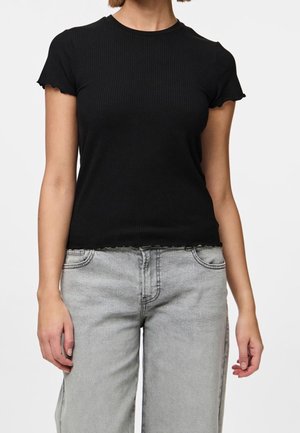 Kobieta ubrana w dopasowany czarny, żeberkowany top z krótkim rękawem z falbankowymi brzegami oraz jasnoszare, wysokowydziarne jeansy z przednimi kieszeniami.