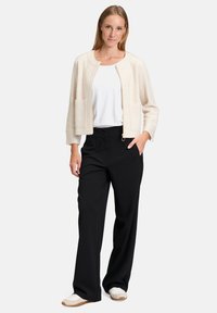 Jasno beżowa krótka kurtka z okrągłym dekoltem i dwoma przednimi kieszeniami. Połączona z czarnymi szerokimi spodniami i białymi trampkami.