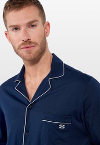 Camisón de color azul marino en material suave, con cuello de solapa, ribetes blancos y un bolsillo con un detalle de logo bordado.