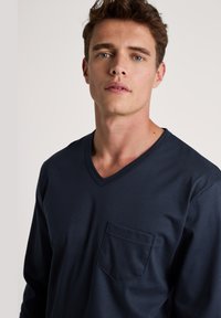 Marineblauwe T-shirt met lange mouwen en V-hals, voorzien van een borstzak en een gladde stofstructuur, ontworpen voor casual draag.