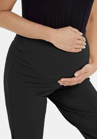 Czarne legginsy ciążowe z elastycznym, prążkowanym pasem. Tkanina jest dopasowana, gładka i ma miękką teksturę, zapewniając komfort i wsparcie.