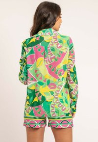 Ensemble chemise et short coloré présentant un motif vibrant de feuilles en vert, rose et jaune avec des contours bien définis et une coupe décontractée.