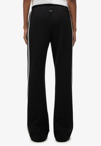 Pantalones deportivos negros con un ajuste relajado, que cuentan con franjas laterales blancas, cintura elástica y tela suave y texturizada. Acentuados por un pequeño logo.