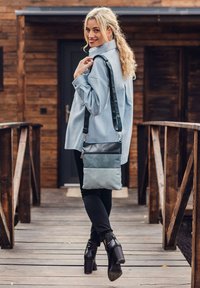 Umhängetasche aus zweifarbigem Teal und schwarzem Material, mit strukturiertem Oberflächendesign, verstellbarem Schultergurt und Reißverschlussfach.