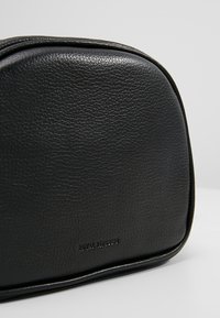 Borsa cosmetica in pelle nera con superficie testurizzata, forma arrotondata e logo in rilievo. Presenta cuciture lisce e chiusura con zip.