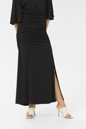 Black maxi dress with ruched detailing, short flared sleeves, and a side slit. Paired with light-colored, open-toe heeled mules.