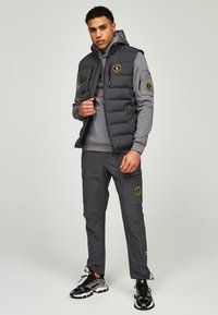 Grijze opblaasbare vest met ritssluiting, gecombineerd met een bijpassende grijze hoodie en cargobroek. Bevat patches en stoffen accenten met textuur.