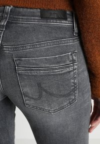 Grijze denimjeans hebben een vervaagde afwerking, een achterzak met gebogen stiksel en een gehaakte bruine sweater. Het LTB-logo is zichtbaar.